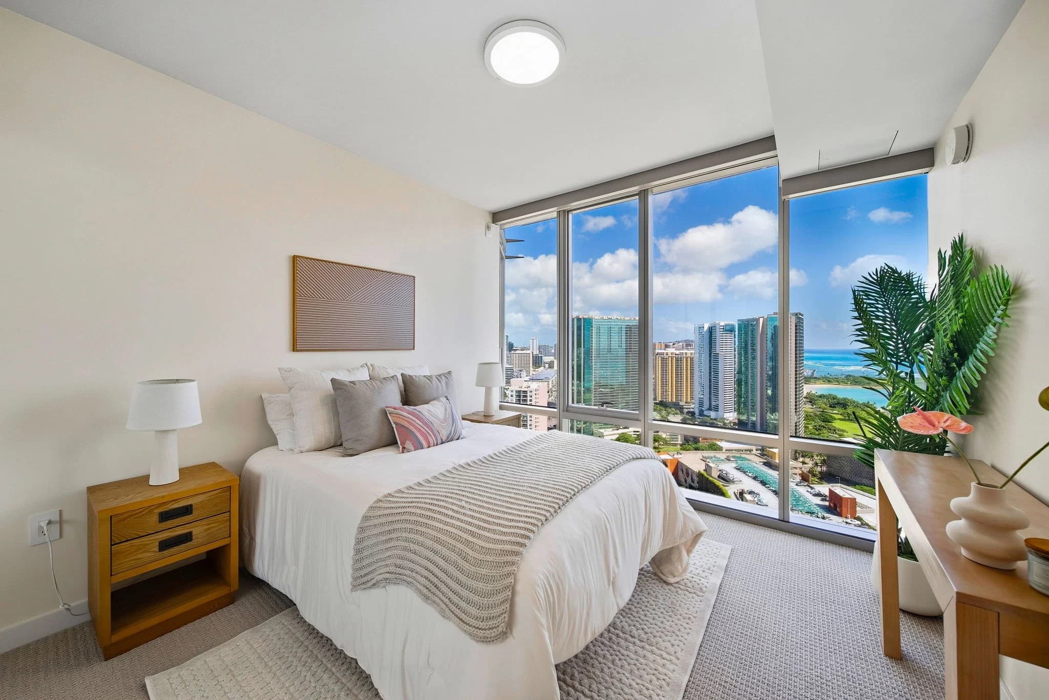 Primary bedroom with floor-to-ceiling windows framing ocean and city views.