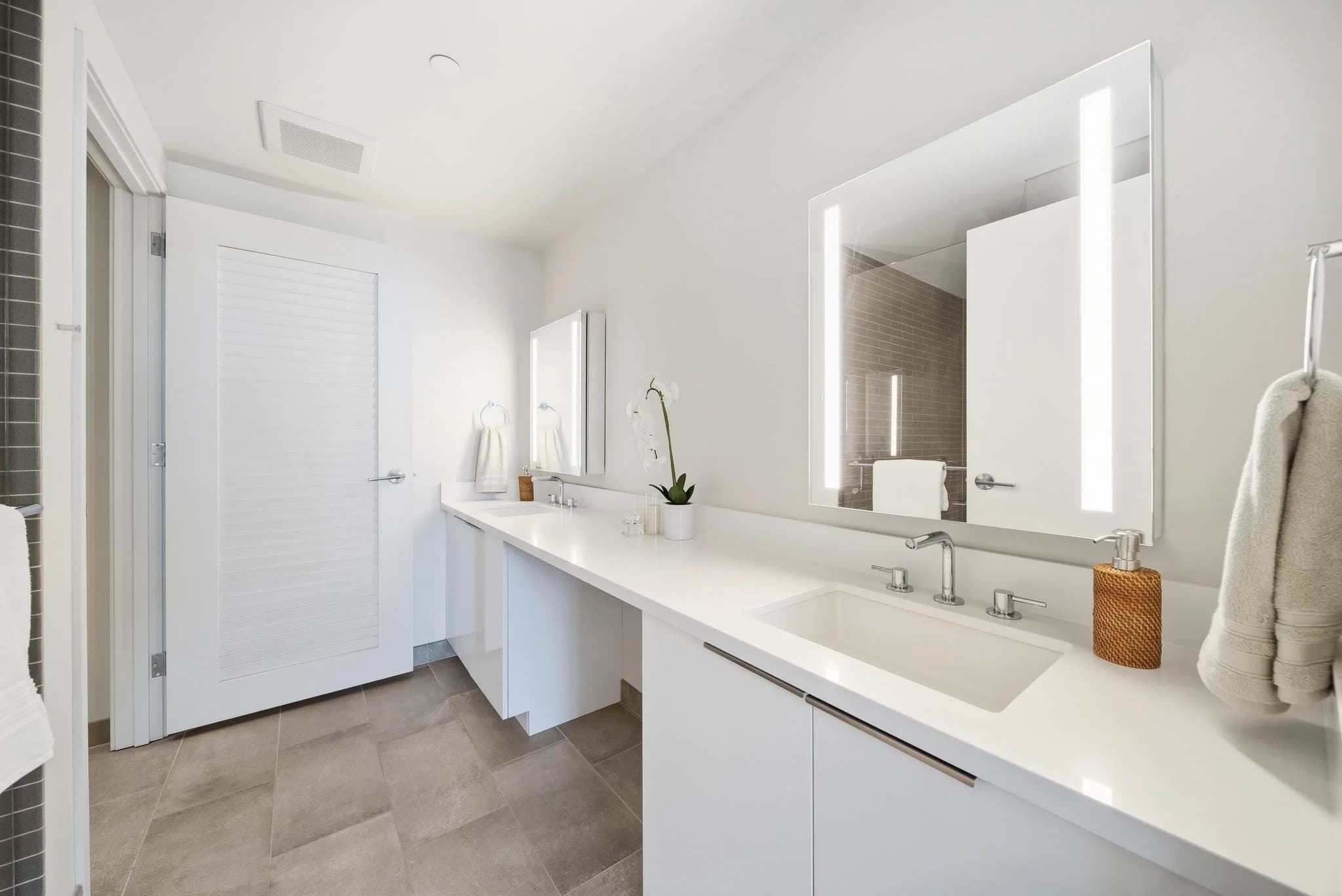 Bathroom with a vanity, quartzite counter, and a backlit mirror.